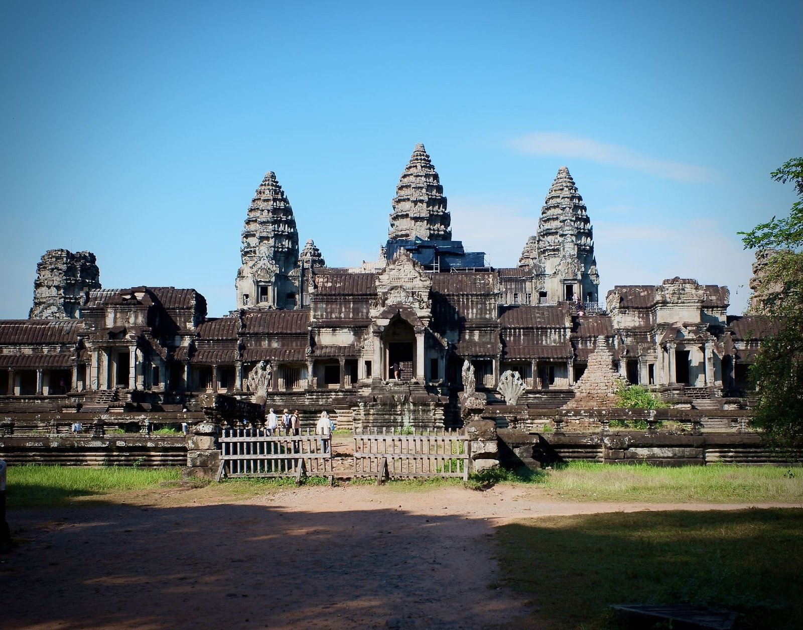 The full front facade of Angkor Wat under a clear blue sky, its five towers rising above the outer galleries