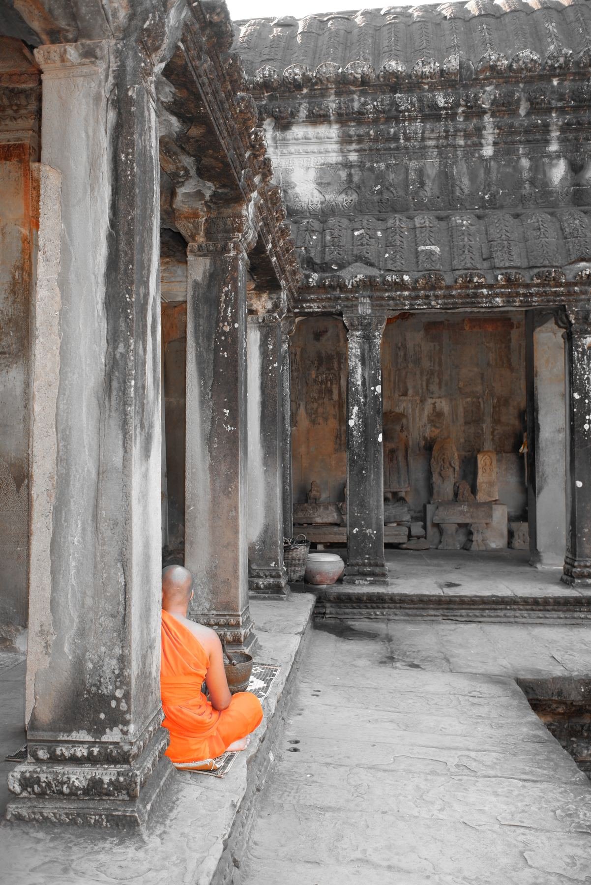 A Buddhist monk in an orange robe sits quietly in a temple corridor