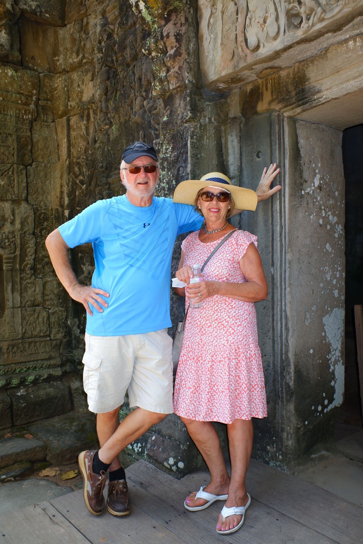 A couple leaning against an ancient carved temple wall, smiling for the camera