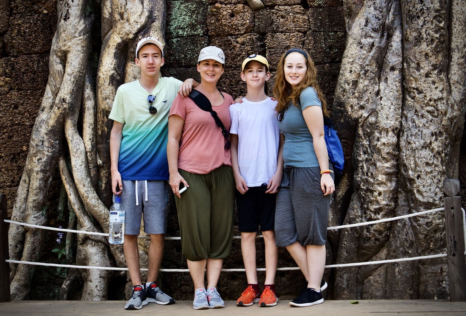 Four family members standing together in front of massive tree roots at Ta Prohm temple