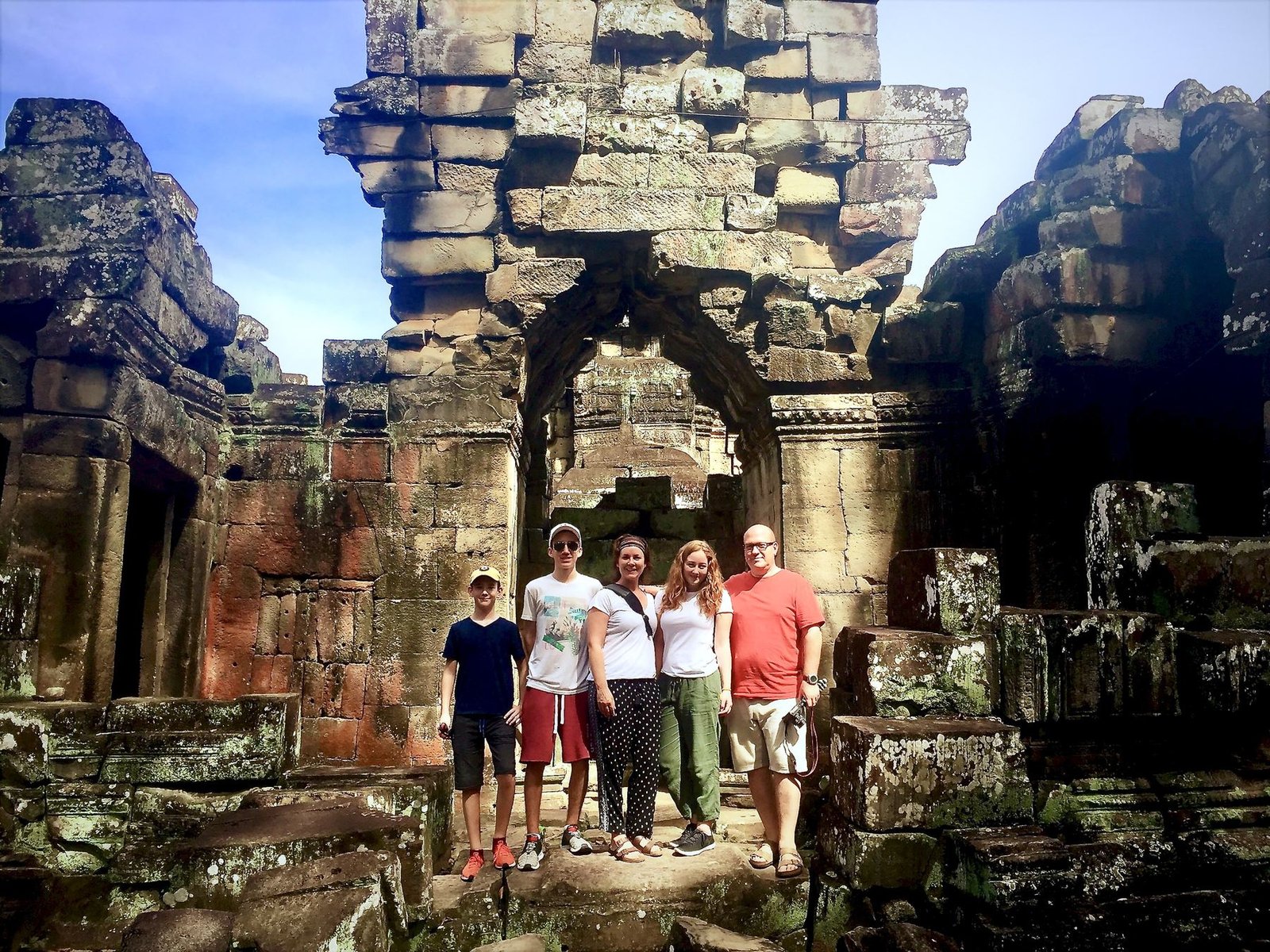 A family of five poses together beneath a stone archway inside a temple ruin